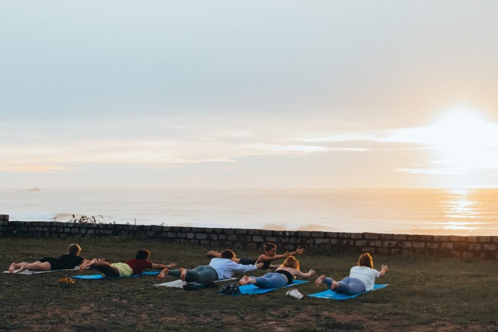 Pessoas fazendo aula de yoga ao nascer do sol com vista para o mar.