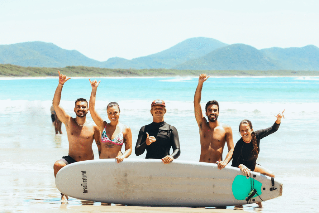 grupo de pessoas sorridentes reunidas na praia, com o mar ao fundo, antes de uma aula de surf