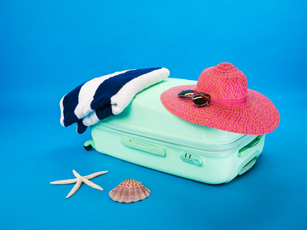 conjunto de mala, toalha, chapéu e óculos, organizados de maneira harmônica, com uma estrela do mar e concha, fazendo analogia a uma viagem praiana.